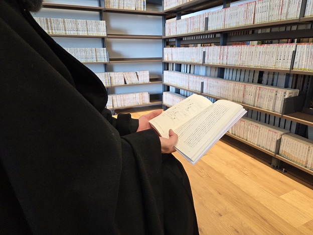 本棚の前で読書するLSの手元を写した写真